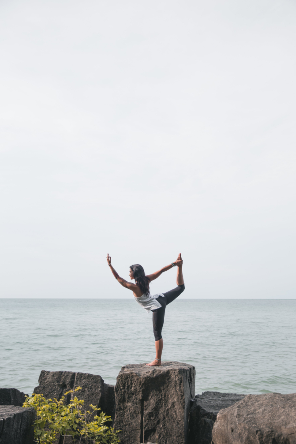 A woman holding a standing balance pose by the sea